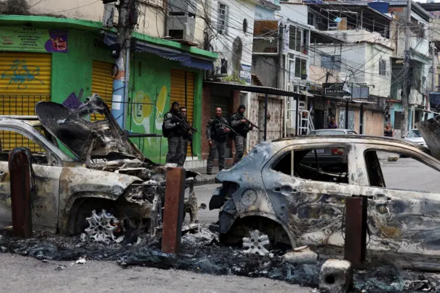 Miembros de la unidad especial de la policía militar patrullan una calle durante un operativo policial contra el narcotráfico. Están detrás de dos autos incendiados en la favela de Penha, en Río de Janeiro.