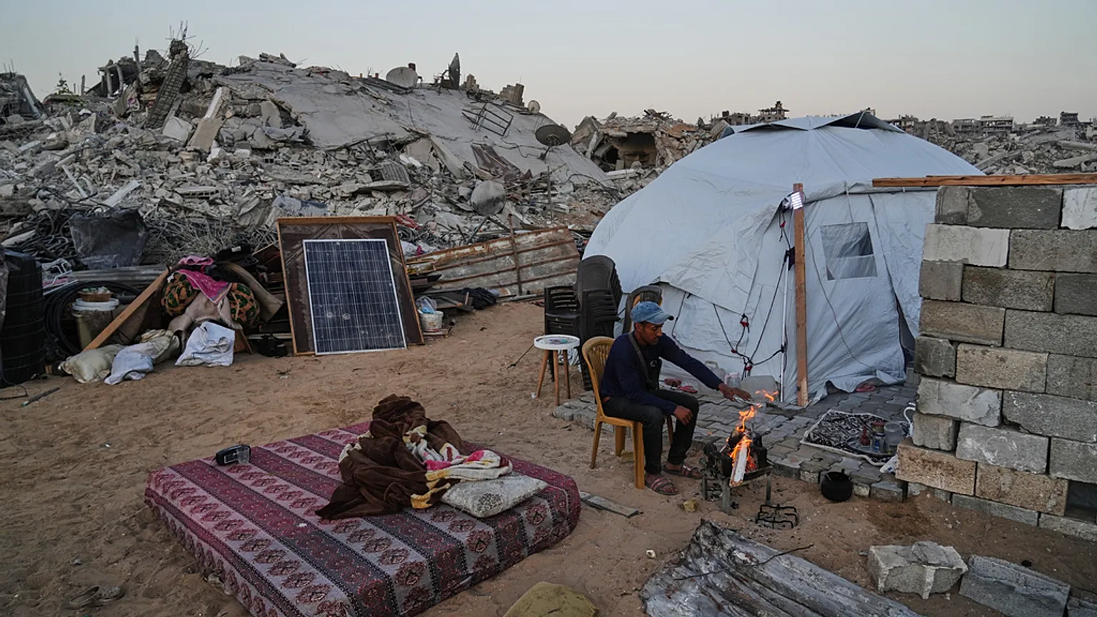 Displaced Palestinian Belal Al-Yaziji sits by a fire outside his tent amid the destruction left by the Israeli air and ground offensive in Sheikh Radwan neighborhood.