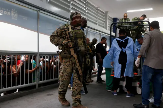 La gente observa cómo miembros de la policía militar trasladan cadáveres a un hospital.
