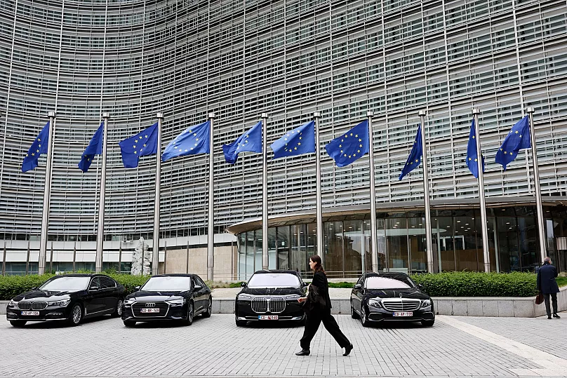 European Union flags flap in the wind as a woman walks past diplomatic vehicles outside the EU headquarters in Brussels, 27 May, 2025