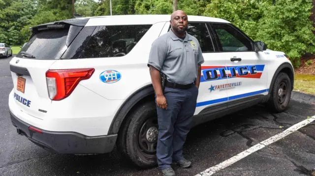 Ly Jamaal Littlejohn posa frente a un auto de policía.