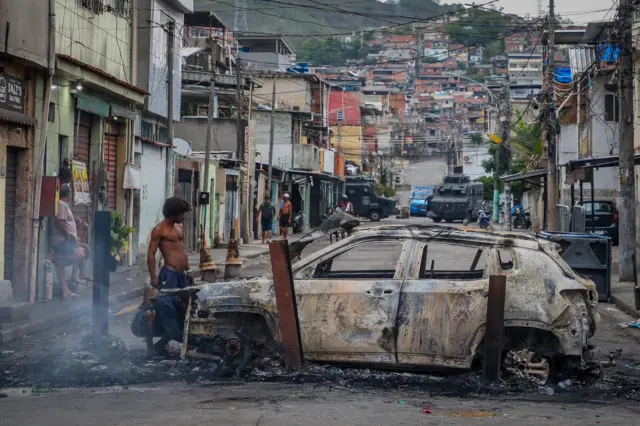 Un hombre observa un coche calcinado que bloquea la calle durante un operativo en Río.