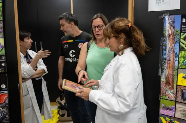 Marisa Vázquez de Agredos, con bata blanca, recoge una fotografía que le entrega una mujer con camiseta verde ante otros miembros del equipo.
