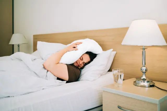 Mujer acostada en la cama con una almohada sobre la cabeza
