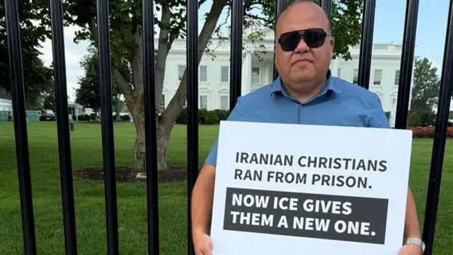 Torosian, con anteojos oscuros, está frente a la Casa Blanca, con una cartel que lee: "Los iraníes cristianos huyeron de prisión; ahora ICE les está dando una nueva".