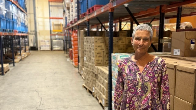 Nelle Miller en un almacén delante de grandes estantes con cajas con productos.