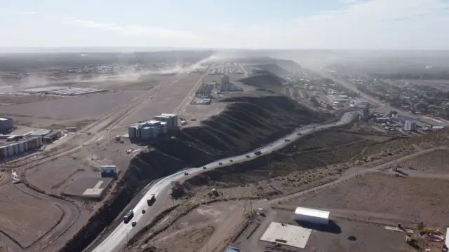 Ruta entre un pueblo con árboles y una meseta árida.