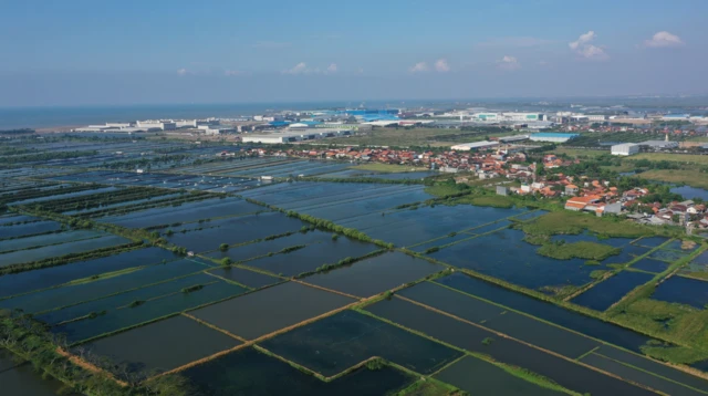 Vista aérea de campos inundados con edificios residenciales e industriales en la distancia.