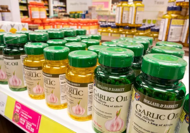 Botellas amarillas y verdes que contienen aceite de ajo y cápsulas con extracto de ajo en un estante 