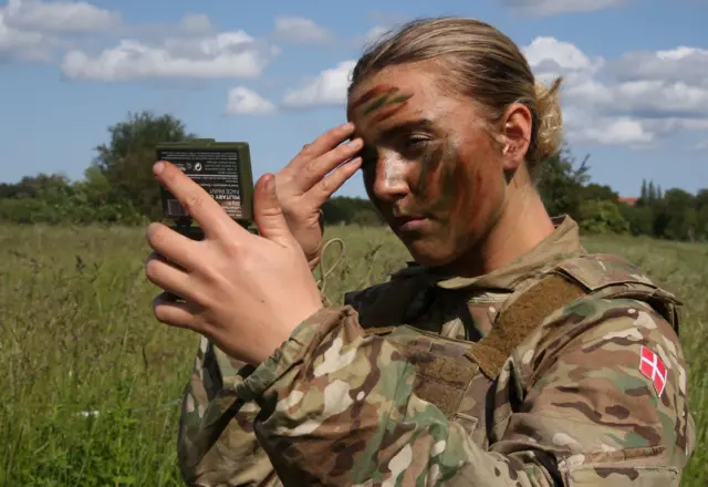 Una soldado de la Guardia Real Danesa se aplica pintura de camuflaje en la cara durante un ejercicio de entrenamiento en Hovelte, Dinamarca, el 11 de junio de 2025.