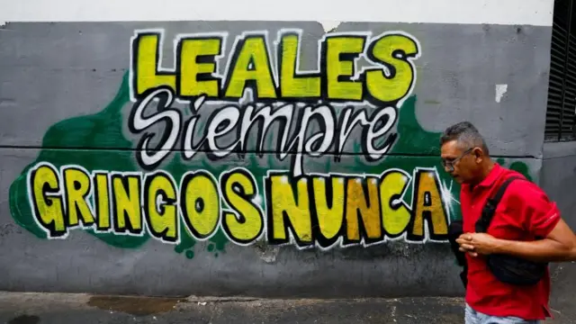 Un hombre camina en una calle de Caracas frente a un mural que dice "Leales siempre, gringos nunca"