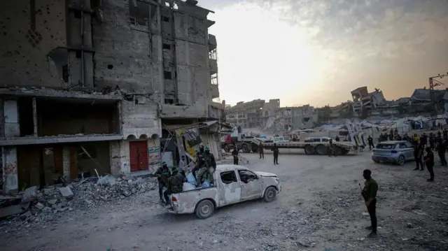 Milicianos de Hamás sentados en la parte trasera de una camioneta, entre edificios destruidos en Ciudad de Gaza. 