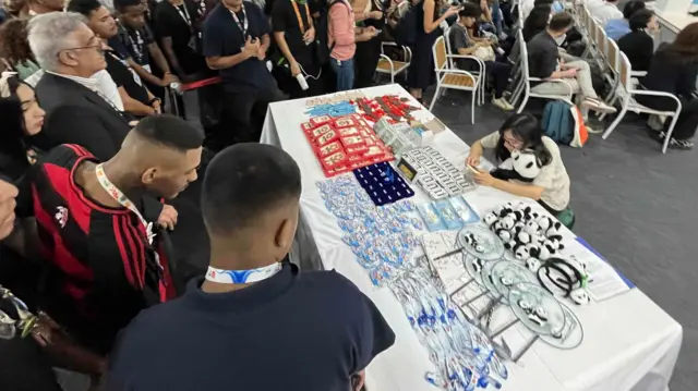 Una multitud rodea una mesa con souvenirs del pabellón de China en la COP30 en Belém, Brasil.