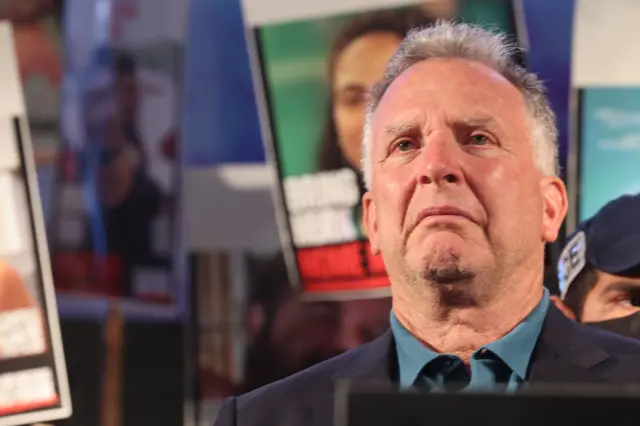 Witkoff mira al frente con semblante serio mientras detrás de él se sostienen pancartas con los rostros de los rehenes israelíes que en ese momento estaban retenidos por Hamás en Gaza.