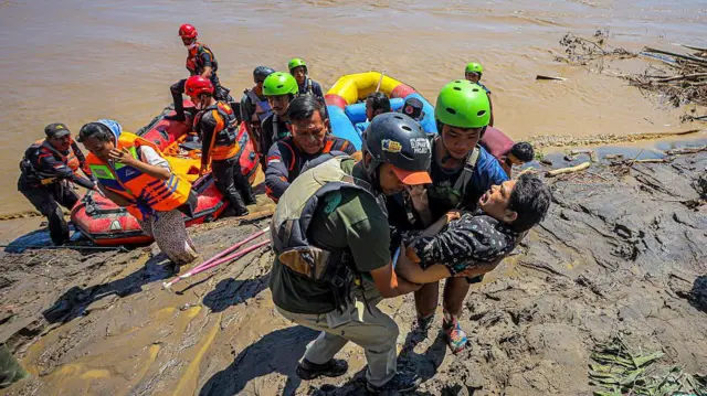 Rescatistas cargan a un hombre de una lancha inflable a una ribera enlodada