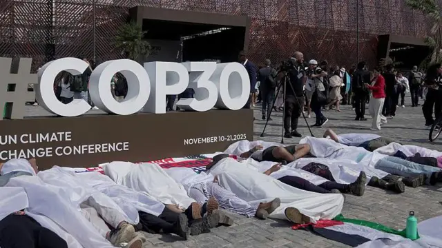 Manifestantes acostados frente a un aviso de la COP30, cubiertos en sábanas blancas.