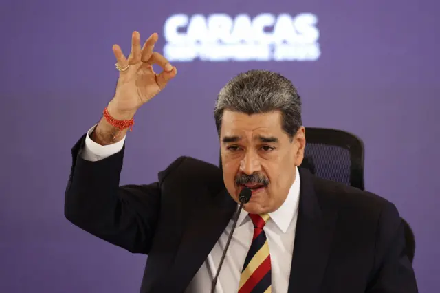 Nicolás Madudo gestigula levantando la mano. Lleva una corbata de rayas.