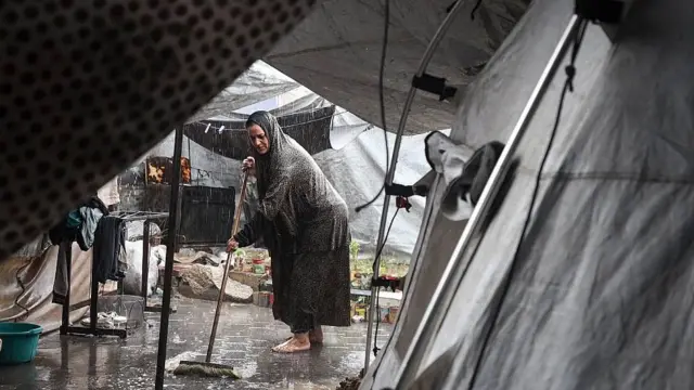 Una mujer descalza intenta barrer el agua que inunda las carpas