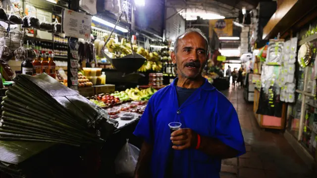 Un hombre en un mercado de Caracas habla mientras sostiene un vaso con café