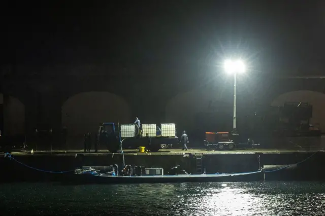 Una imagen de noche de un sumergible en el agua mientras varias personas están descargándolo en un puerto de concreto.