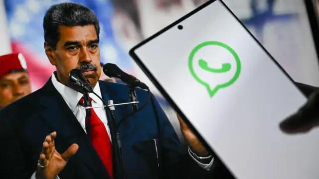 Un teléfono en el que se ve el logo de WhatsApp y detrás una foto del presidente de Venezuela.