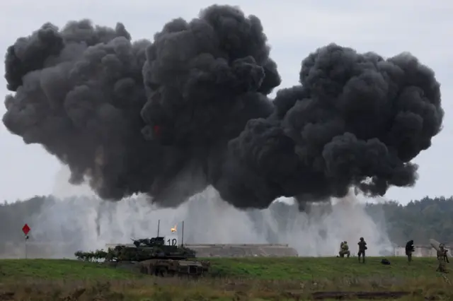 Soldados operan cerca de un tanque Abrams polaco mientras las fuerzas polacas y los soldados de la OTAN realizan maniobras militares en un campo de entrenamiento en Wierzbiny, cerca de Orzysz, Polonia, el 17 de septiembre de 2025. Se puede ver una gran nube de humo negro sobre el tanque, con los soldados recortados contra el humo gris más claro cerca del suelo.