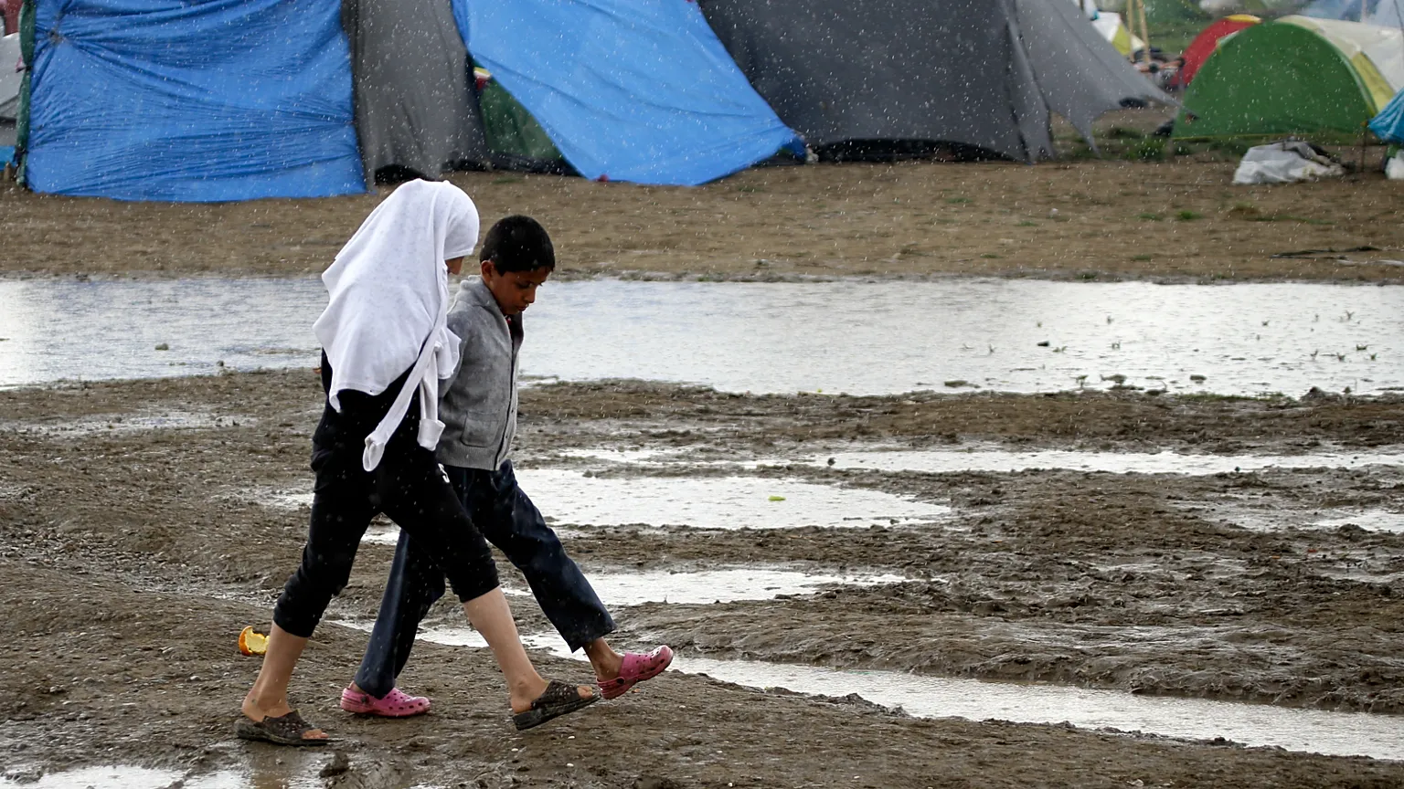 Children walk across a muddy filed at the northern Greek border point of Idomeni, Greece, Monday, April 25, 2016.