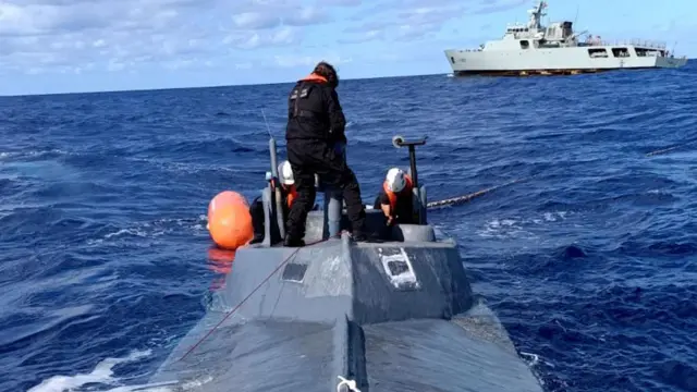 Un submarino en el mar con un buque de la armada portuguesa al fondo.