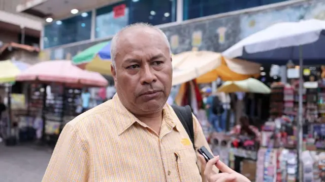Javier Jaramillo mira hacia la entrevistadora frente a algunos puestos de comerciantes en Caracas