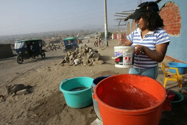 Una mujer junto a cubos de agua en una calle sin asfaltar de Perú.