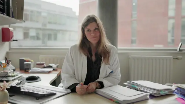 La doctora Kasper sentada en su mesa de despacho con una bata blanca. 