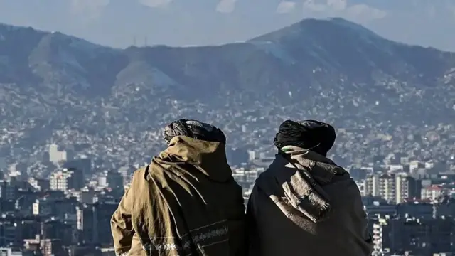Dos miembros del Talibán de espaldas en una cima observando Kabul