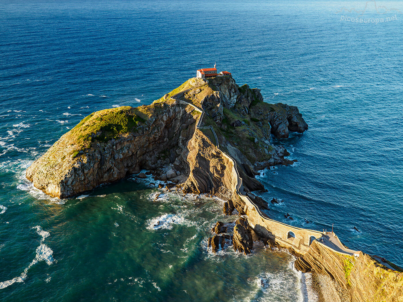 Foto: Una ermita corona la cima de un escarpado islote unido a la costa por un serpenteante puente de piedra, en Vizcaya. (Extraída de Facebook)