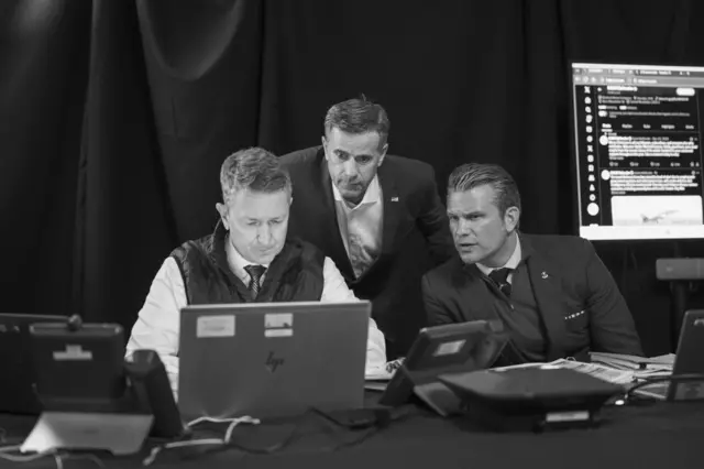 Ratcliffe y Hegseth miran una laptop en la que trabaja un funcionario.