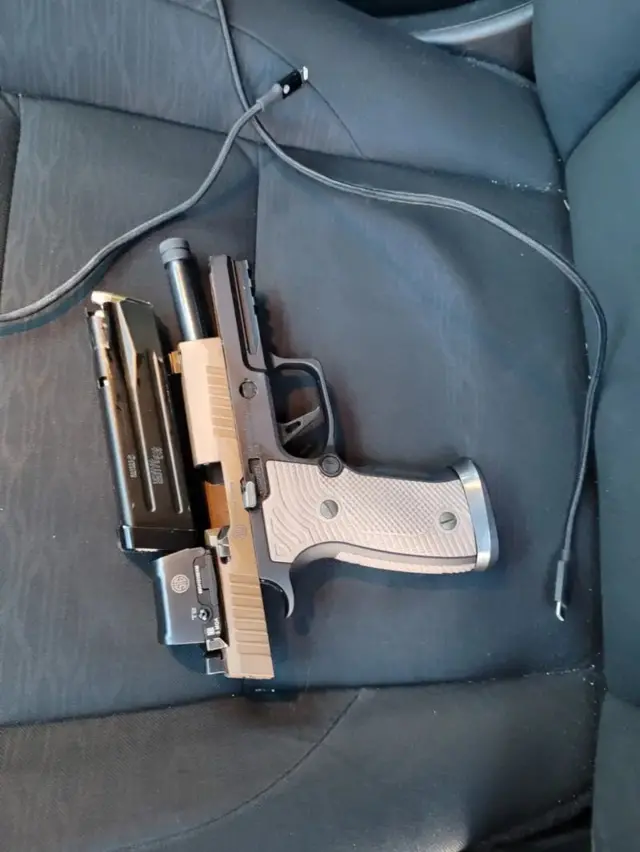 Una pistola semiautomática de 9 mm colocada en el asiento de un coche con un cable de carga al lado del arma.