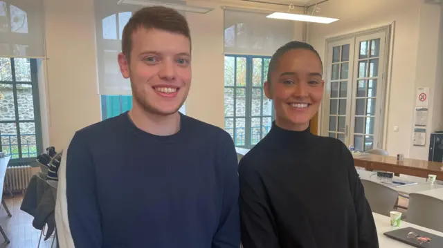 Los estudiantes Alexandre Hubert y Valentine Guillot sonríen a la cámara mientras están de pie en un aula.