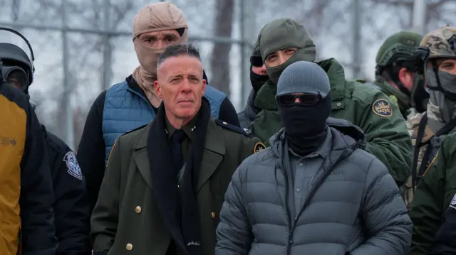 El jefe de patrulla de la Patrulla Fronteriza de EE. UU., el agente Gregory Bovino (C), se encuentra entre agentes del Departamento de Policía de Minneapolis y agentes federales durante una protesta contra ICE frente al Edificio Federal Whipple, una base para operaciones federales de control migratorio, en Fort Snelling, Minnesota, EE. UU., el 15 de enero de 2026. Foto de OLGA FEDOROVA/EPA/Shutterstock
