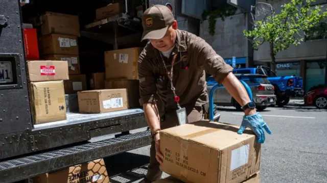 Empleado de UPS carga una caja detrás de un camión lleno de paquetes.