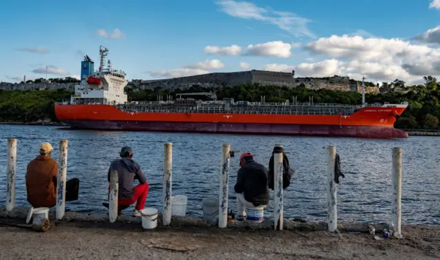 Un barco petrolero en la costa de La Habana y hombres pescadores viéndolo de espaldas