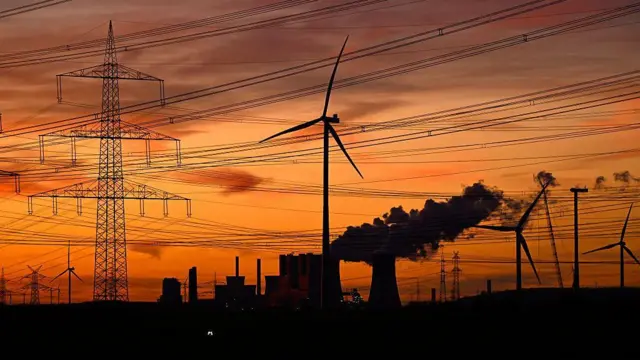 Esta fotografía, tomada al atardecer del 12 de noviembre de 2025, muestra aerogeneradores y postes de luz mientras se elevan los humos de las torres de refrigeración de la central termoeléctrica de lignito operada por el gigante energético alemán RWE, cerca de Neurath, en el oeste de Alemania.