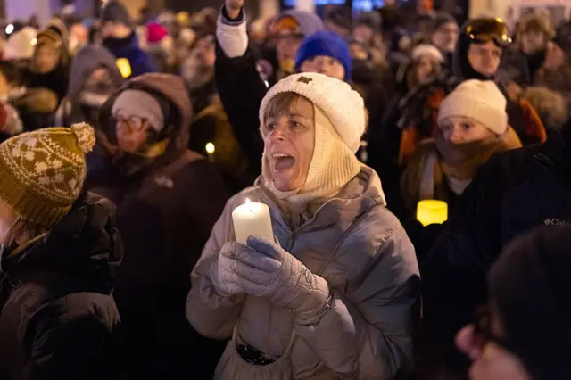 Personas asisten a una vigilia con velas organizada por personal sanitario en el lugar donde Alex Pretti fue asesinado el 24 de enero de 2026 en Minneapolis, Minnesota. Van vestidas con mucha ropa de abrigo: chaqueta, grandes guantes, pasamontañas, gorros. Llevan velas en sus manos.