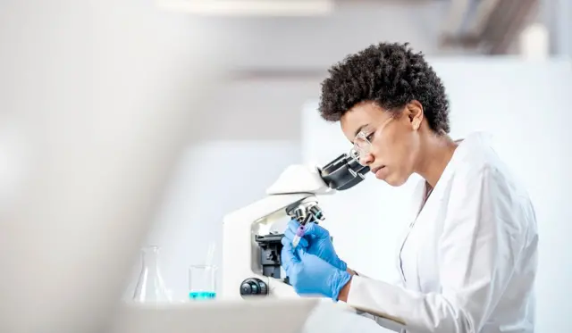 Una investigadora con guantes azules ve una muestra en un microscópio