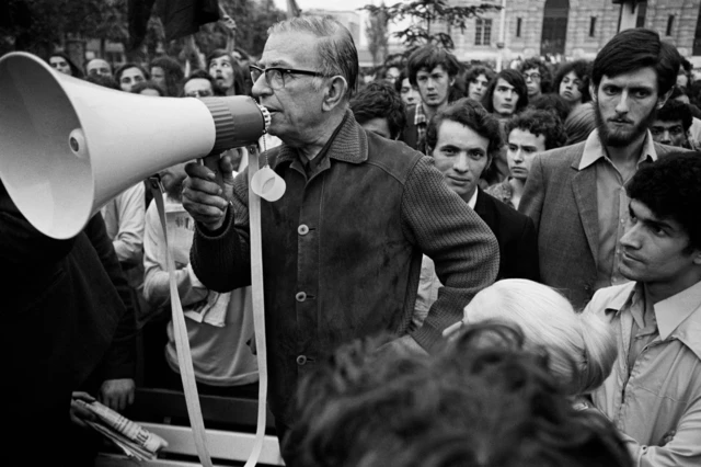 Sartre con un saco de botones, en la calle, rodeado de jóvenes, mientras hablaba con un altoparlante.