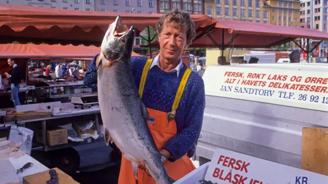 Un pescadero que sostiene un salmón grande en el mercado de Bergen, Noruega