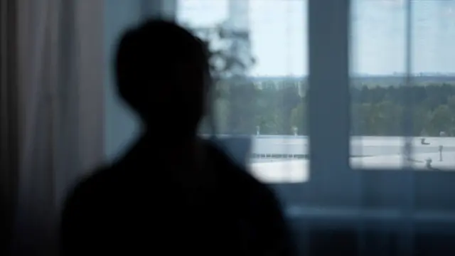 La identidad de Mariyana está protegida en la imagen. Su silueta negra mira hacia una ventana con vistas a los árboles verdes.