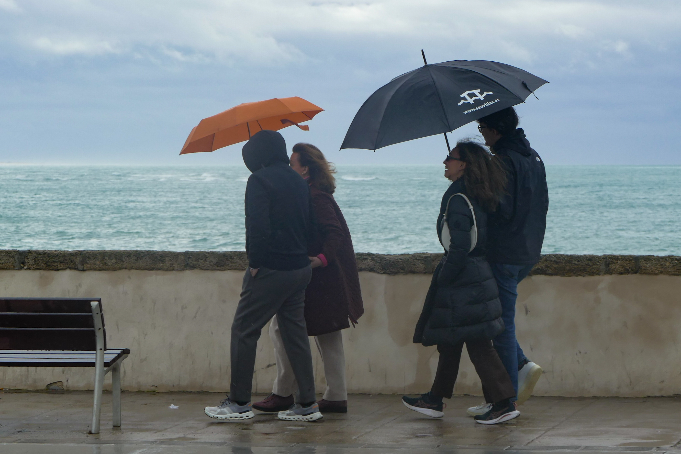 Varias personas se protegen de la lluvia mientras pasean por el Campo del Sur, en Cádiz.