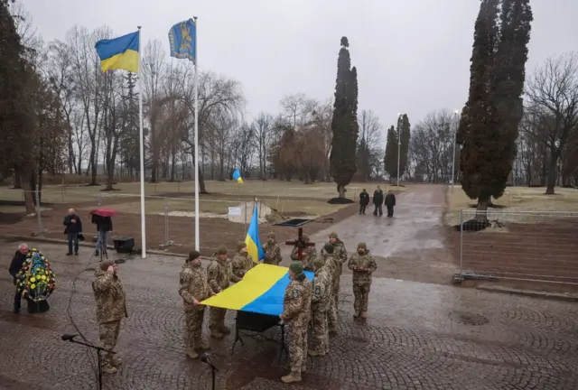 Soldados uniformados sostienen una bandera ucraniana sobre un ataúd en el funeral de un soldado.