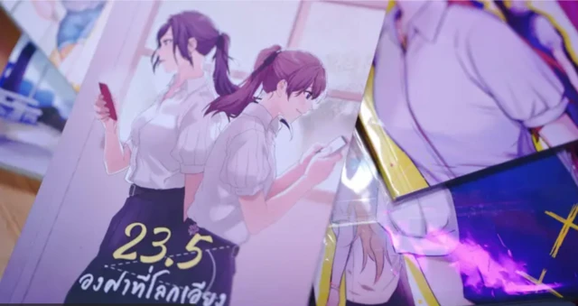 La pareja de GL que protagoniza la serie tailandesa “23,5 grados de inclinación de la Tierra” está representada en el estilo manga, cada una mirando alegremente su teléfono celular mientras se cruzen en el camino frente a una gran vitrina