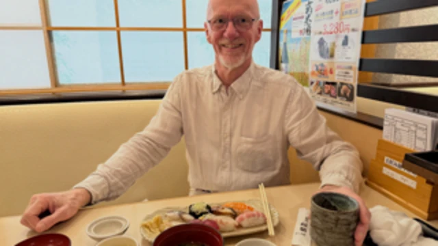 Bjørn-Eirik Olsen está sentado a una mesa con un plato de sushi delante. Vestido con una camisa blanca y sosteniendo una taza, mira directamente a la cámara.