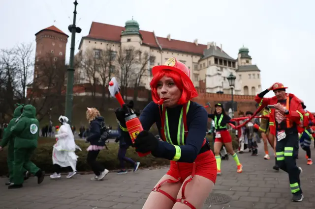 Personas disfrazadas con diferentes trajes, incluyendo bomberos y bomberas, participan en la carrera de Nochevieja en Cracovia, Polonia.